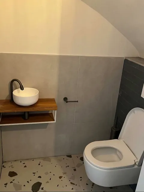 Toilet onder een schuine wand met fonteintje op houten plank