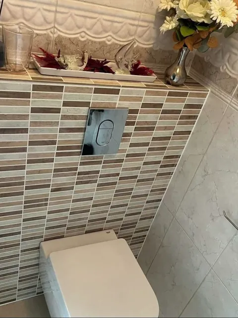 Hangtoilet voor een wand met mozaiektegels en een bedieningsplaat